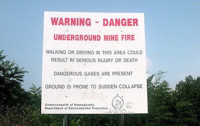 Sign that reads: Warning - Danger. Underground mine fire. Walking or driving in this area could result in serious injury or death. Dangerous gases are present. Ground is prone to sudden collapse.