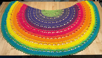 a crocheted shawl in the shape of a semi-circle in a rainbow gradient of colors